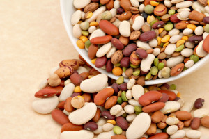 Assorted dry beans spilling from a dish resting on textured paper.